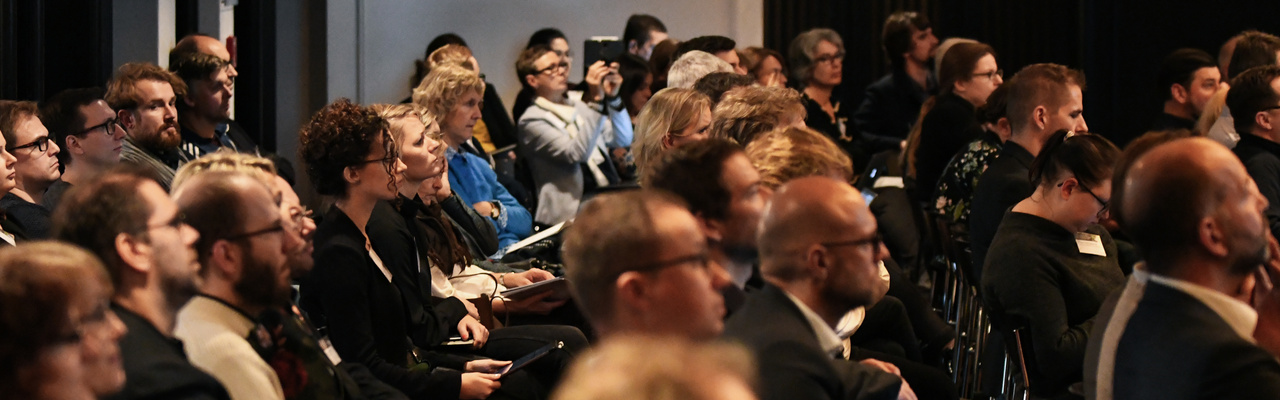 Titelbild Campus Innovation Menschen sitzen gemeinsam in einem Raum und hören einem Vortrag zu.